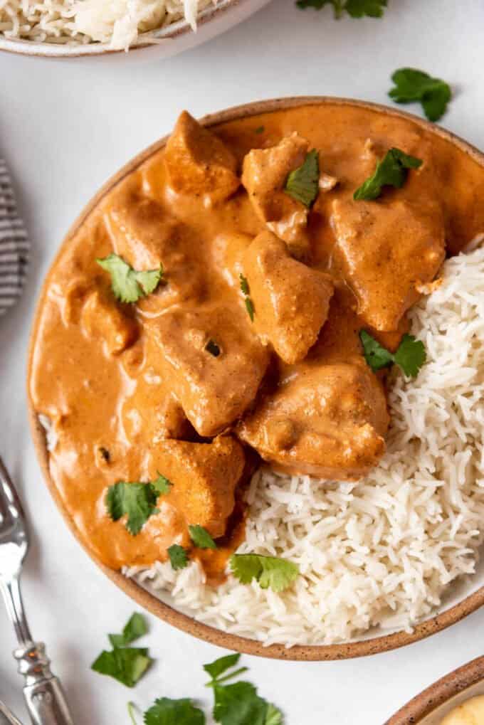 A close image of pieces of tender chicken in a creamy spice tomato curry sauce on a plate with Indian basmati rice.