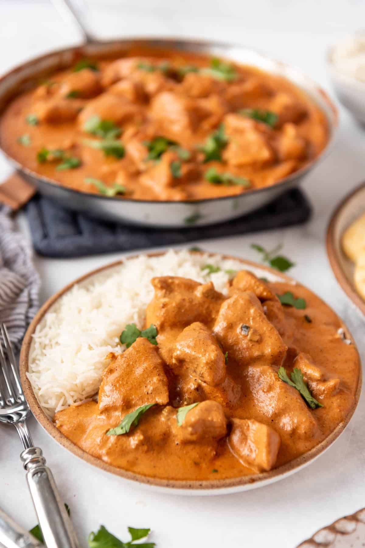 Chunks of chicken in a homemade tikka masala sauce on a plate with white rice.