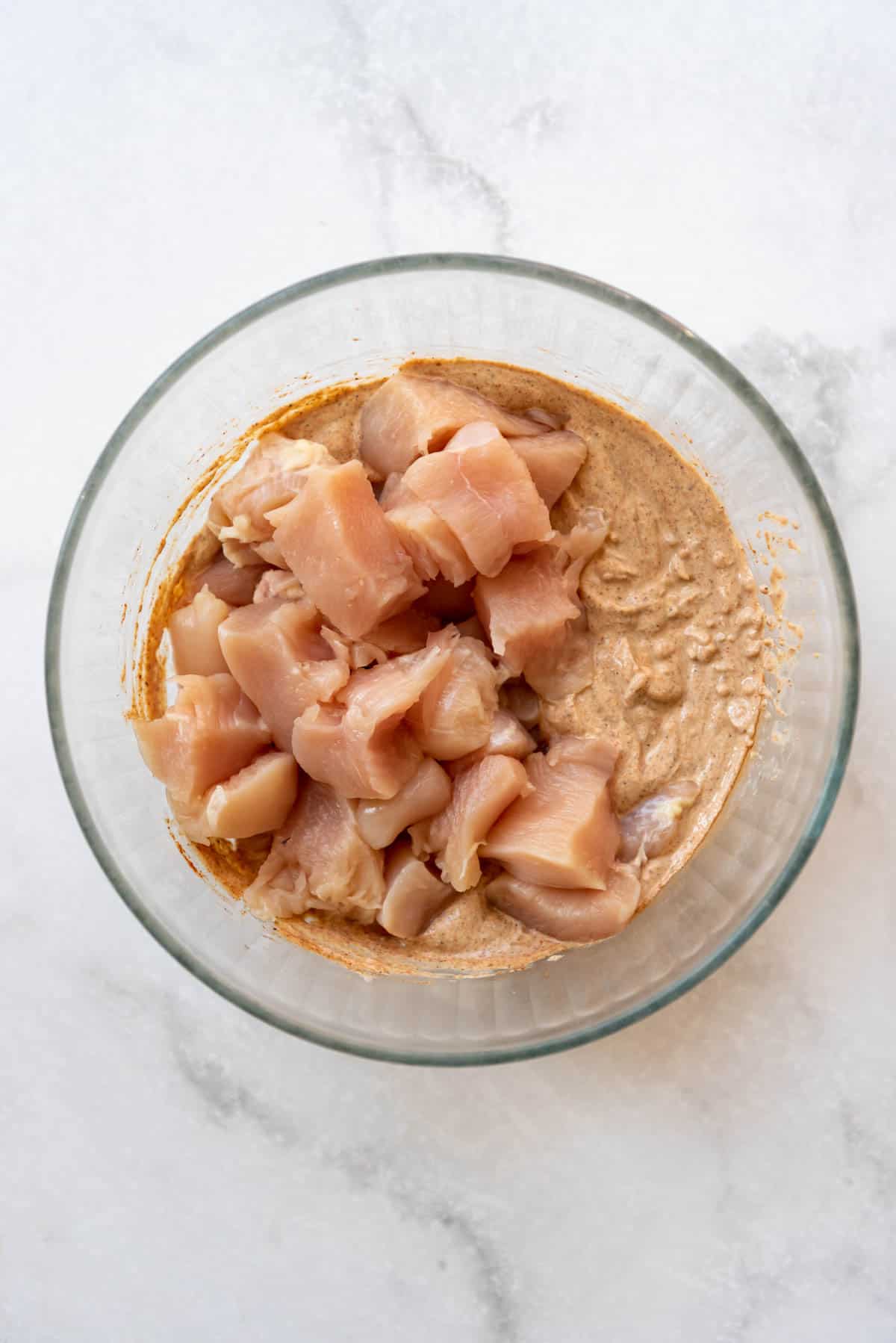 Adding chicken pieces to a large glass bowl with yogurt marinade.