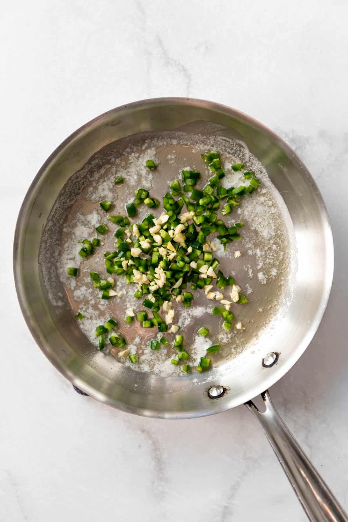 Sauteeing garlic and chopped jalapeno in a large pan with butter.