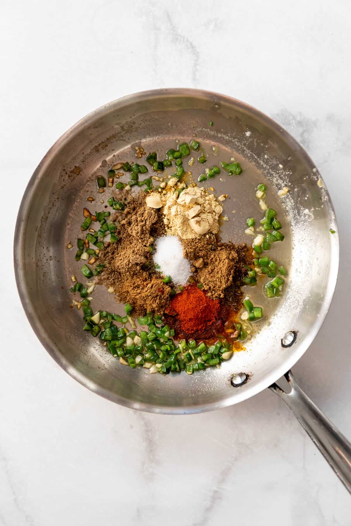 Adding spices to a skillet with sauteed jalapeno and garlic.