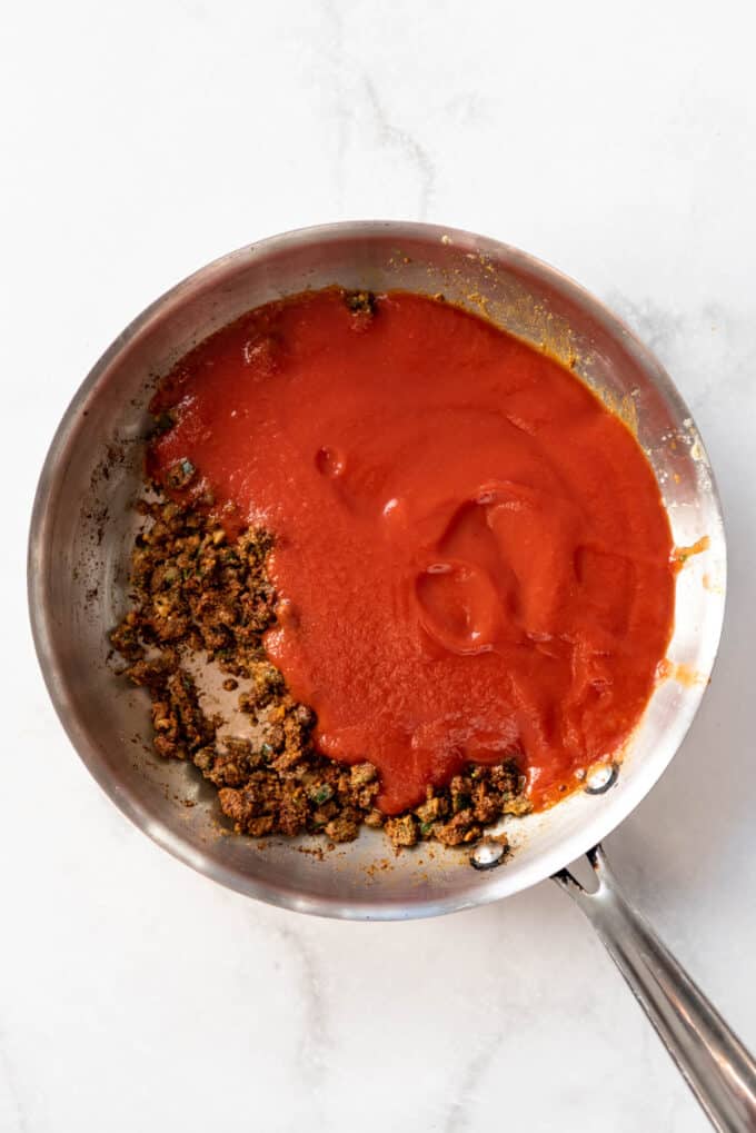 Adding tomato sauce to cooked spices in a pan.