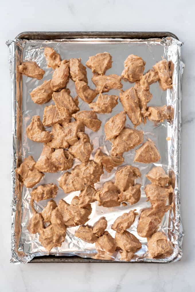 Yogurt and spice marinated chicken pieces on a baking sheet lined with aluminum foil.