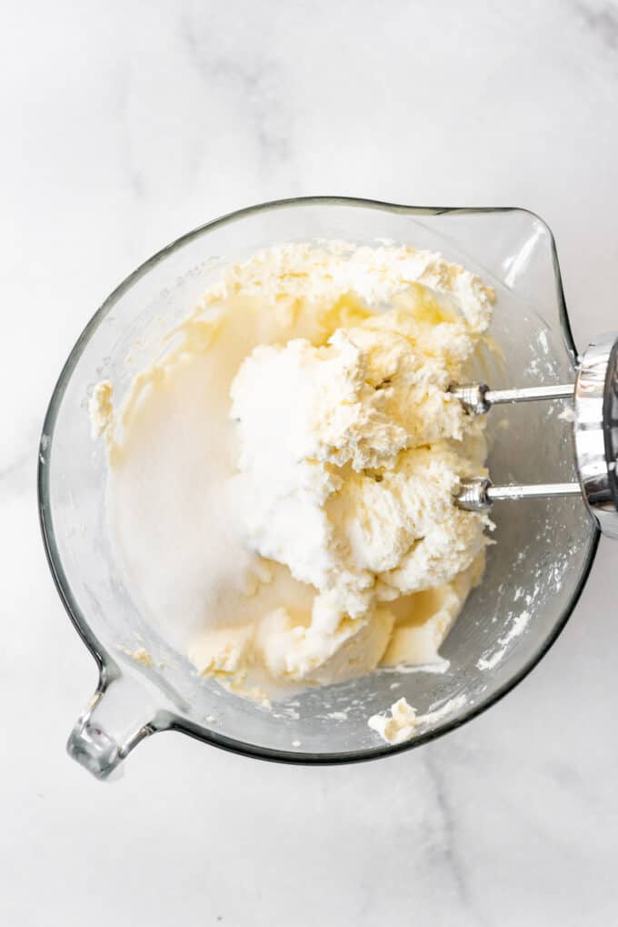 Mixing cream cheese and sugar in a large glass bowl with a hand mixer.