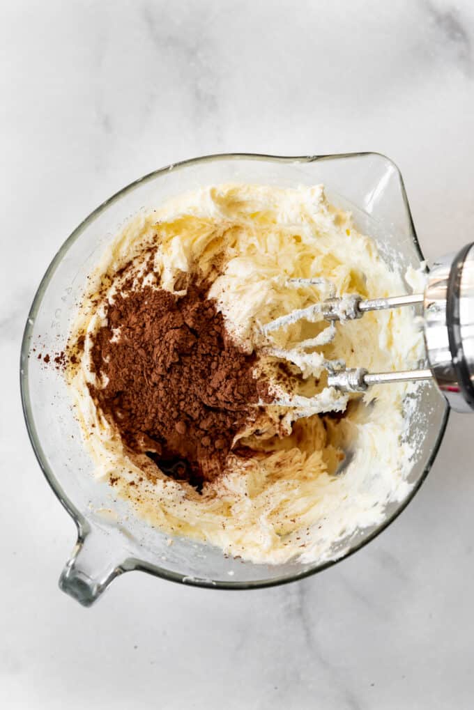 Adding cocoa powder to cheesecake batter in a glass bowl.