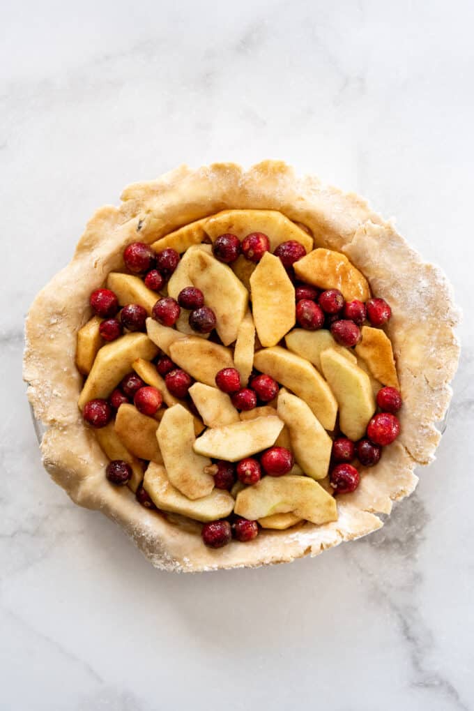 An unbaked pie crust filled with sliced apples and fresh cranberries in sugar, cinnamon, and flour for thickening.