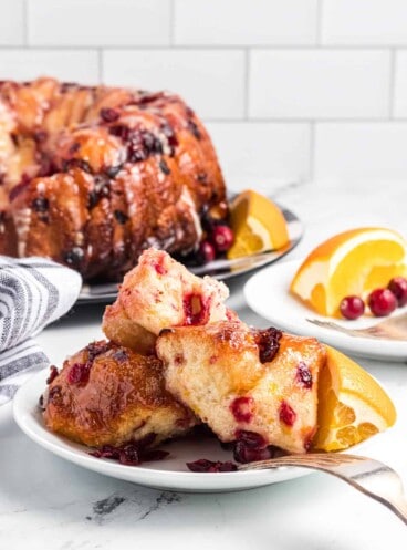 Cranberry orange monkey bread piled on a plate in front of the rest of the monkey bread on a serving plate.