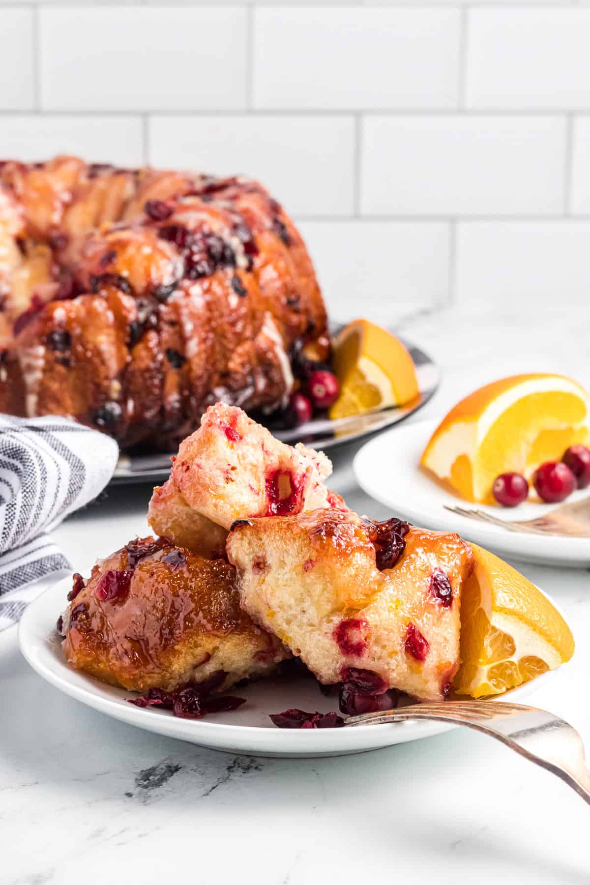Cranberry orange monkey bread piled on a plate in front of the rest of the monkey bread on a serving plate.
