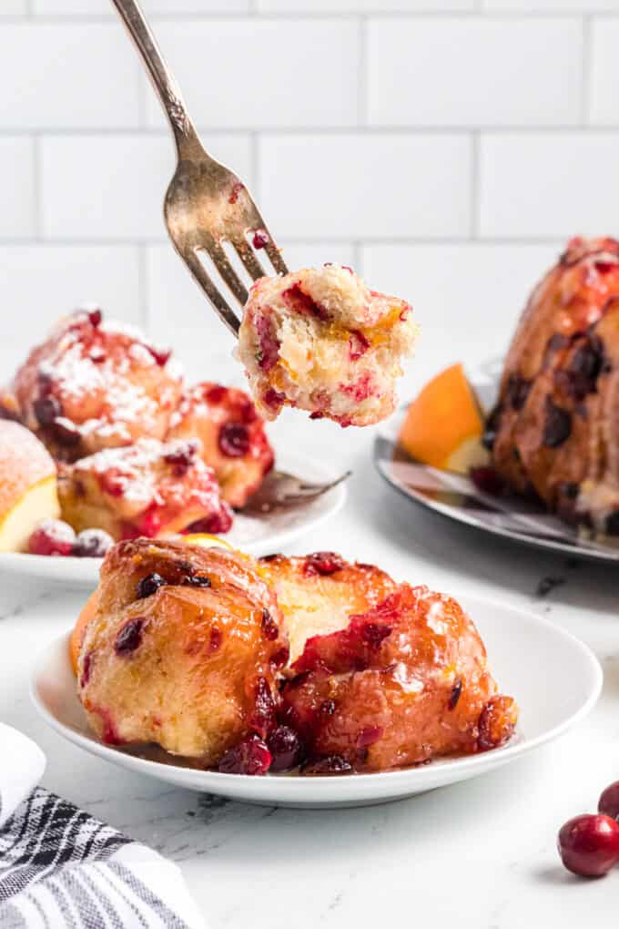 A fork lifting a bite of cranberry orange monkey bread from a white plate.