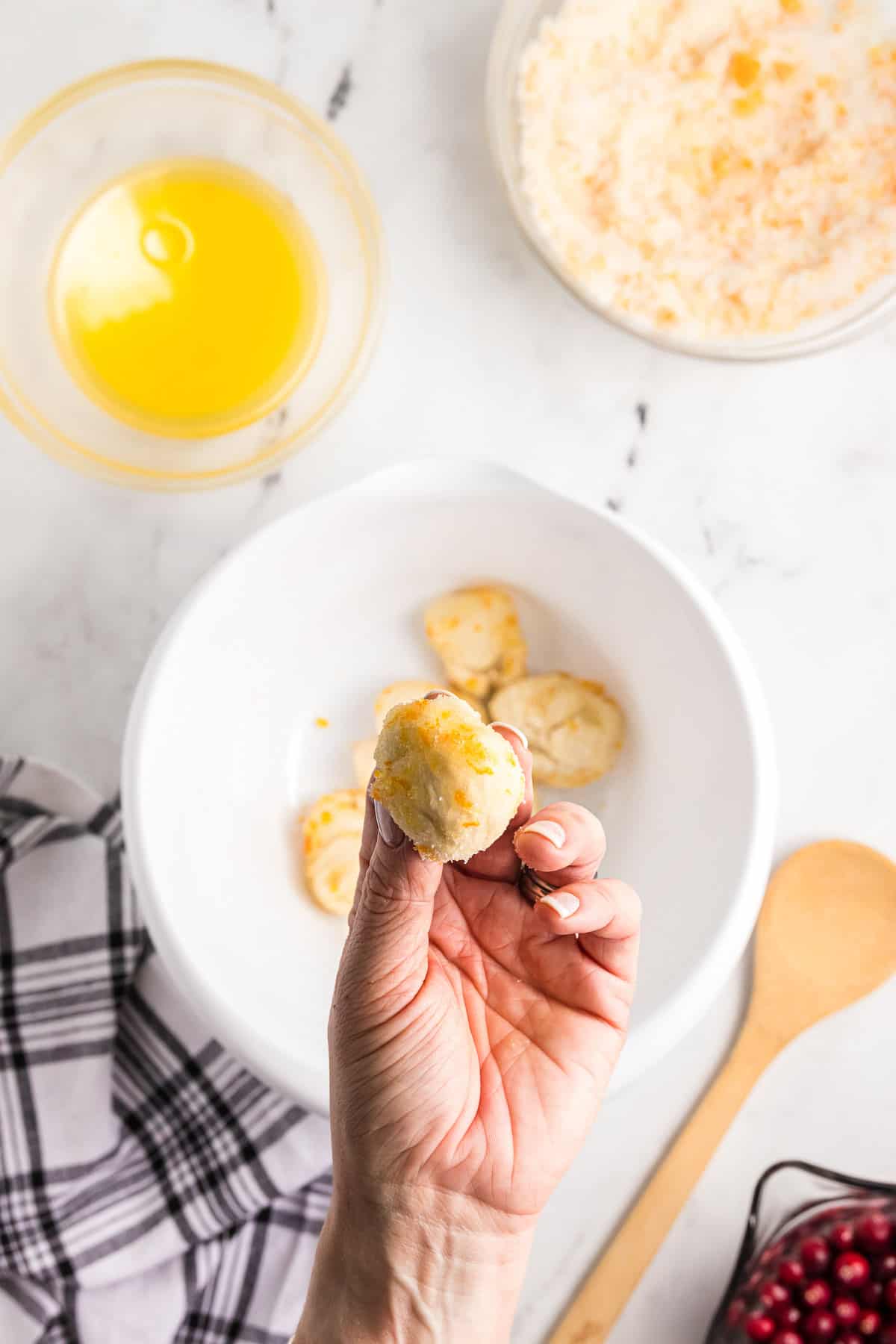 A hand holding a piece of bread dough that has been dipped in butter, sugar, and orange zest.