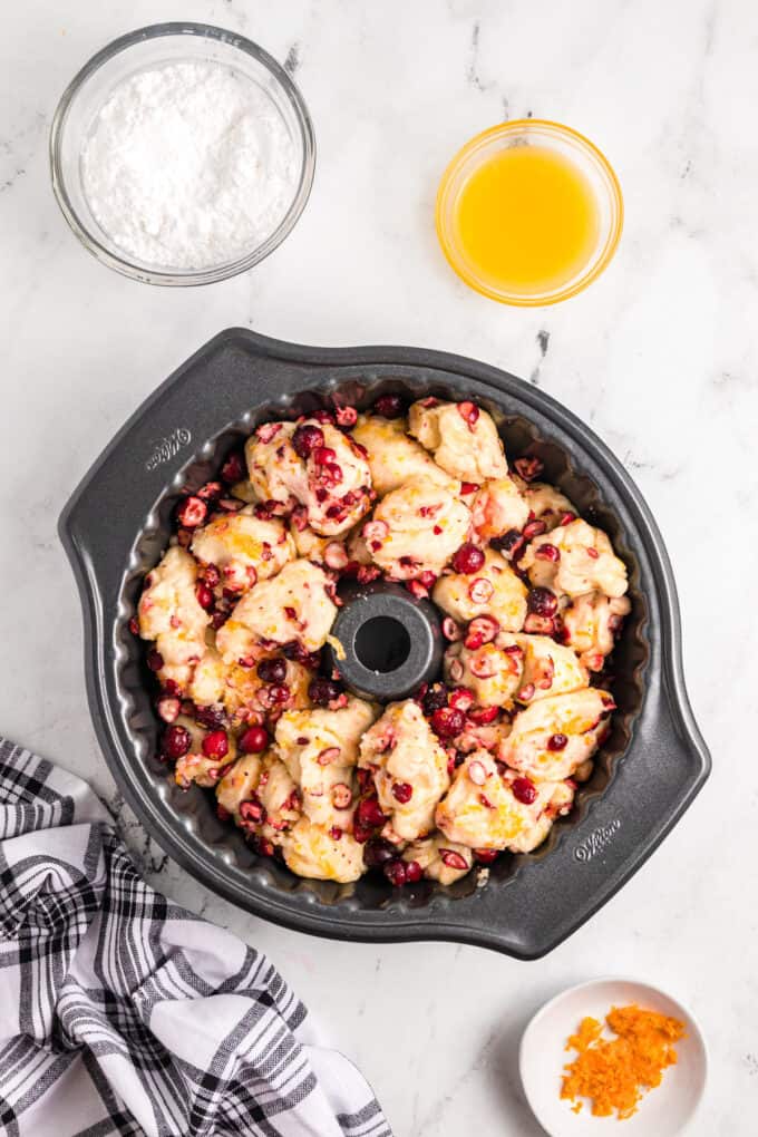Chunks of roll dough in a bundt pan with citrus and sugar coating and chopped fresh cranberries.
