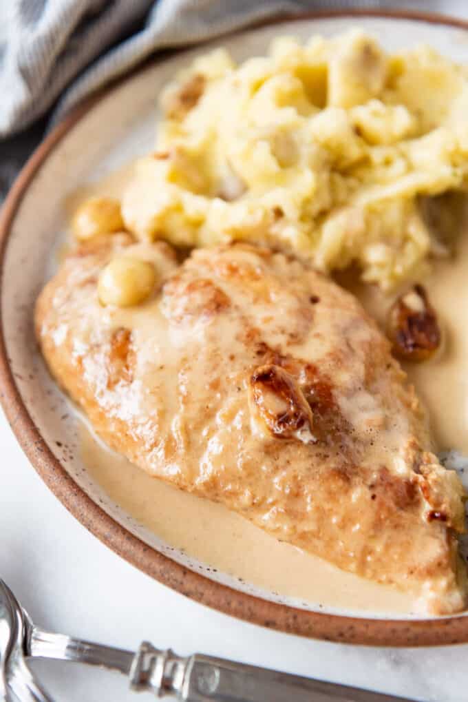 A piece of creamy garlic chicken on a plate next to a pile of mashed potatoes.