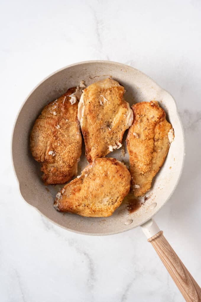 Seared golden brown chicken cutlets in a large pan.