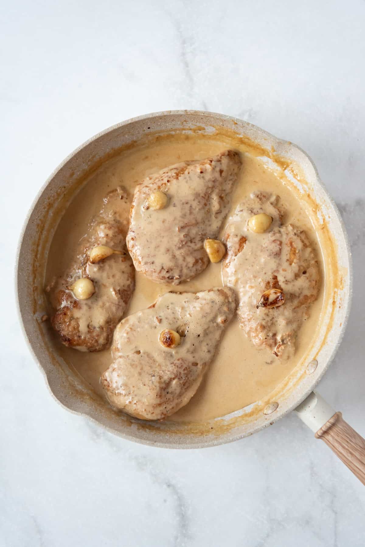 Letting chicken breasts simmer in a pan after adding heavy cream and parmesan to a sauce made from chicken broth and lemon juice.