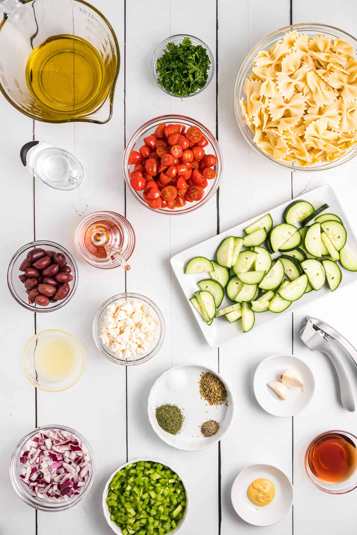 Bowls holding the ingredients for making Greek pasta salad.