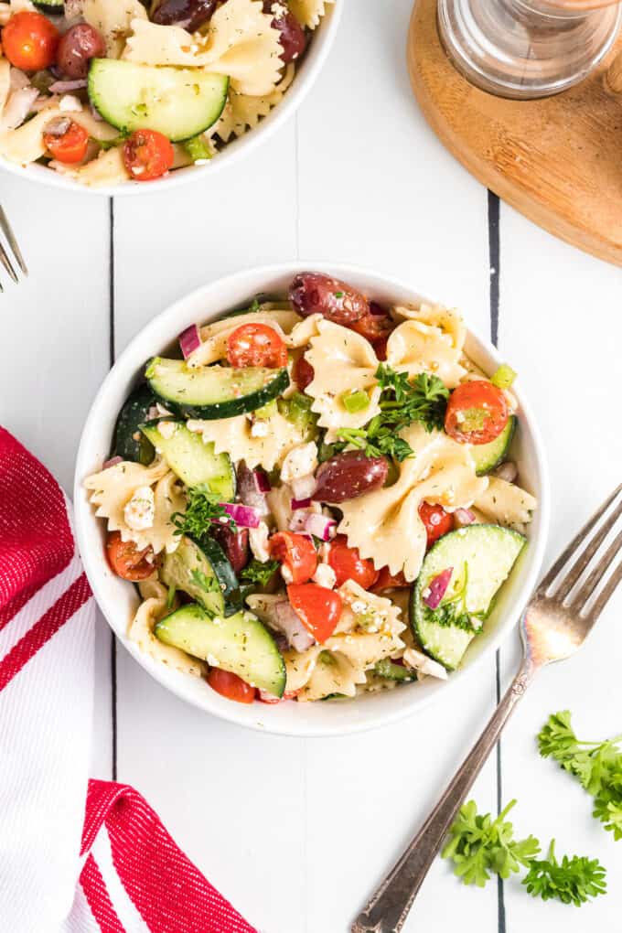 Greek pasta salad with cucumbers and tomatoes in a white bowl.