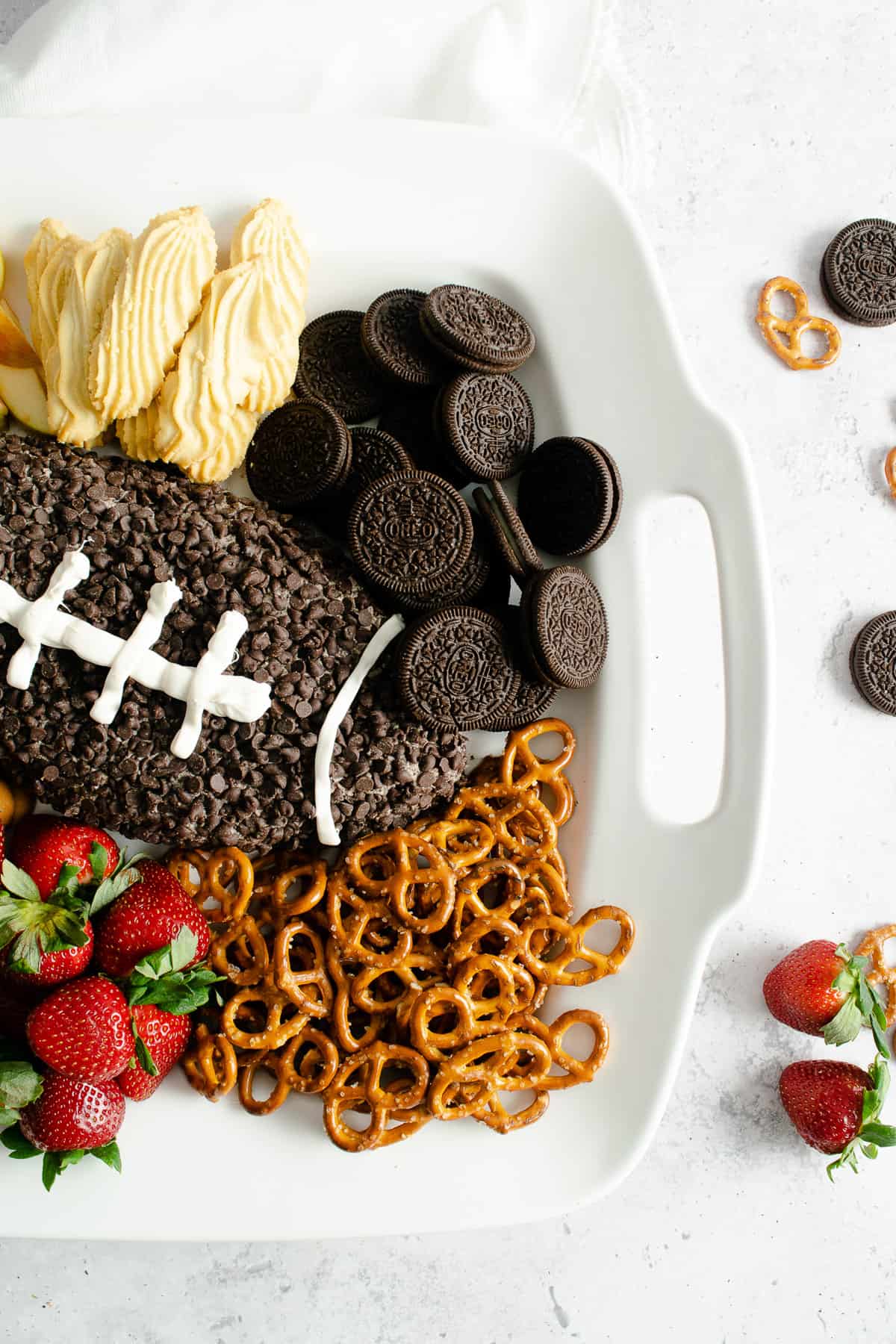 Cookies, pretzels, and strawberries on a white platter surrounding a chocolate cookies & cream dessert cheese ball.