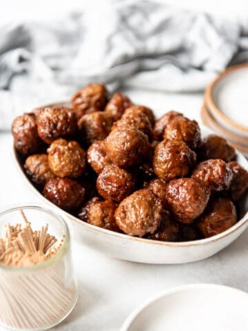 Easy grape jelly appetizer meatballs in a bowl next to a small glass jar of toothpicks for serving.