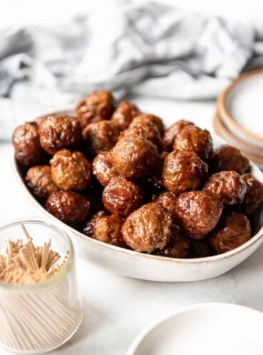 Easy grape jelly appetizer meatballs in a bowl next to a small glass jar of toothpicks for serving.