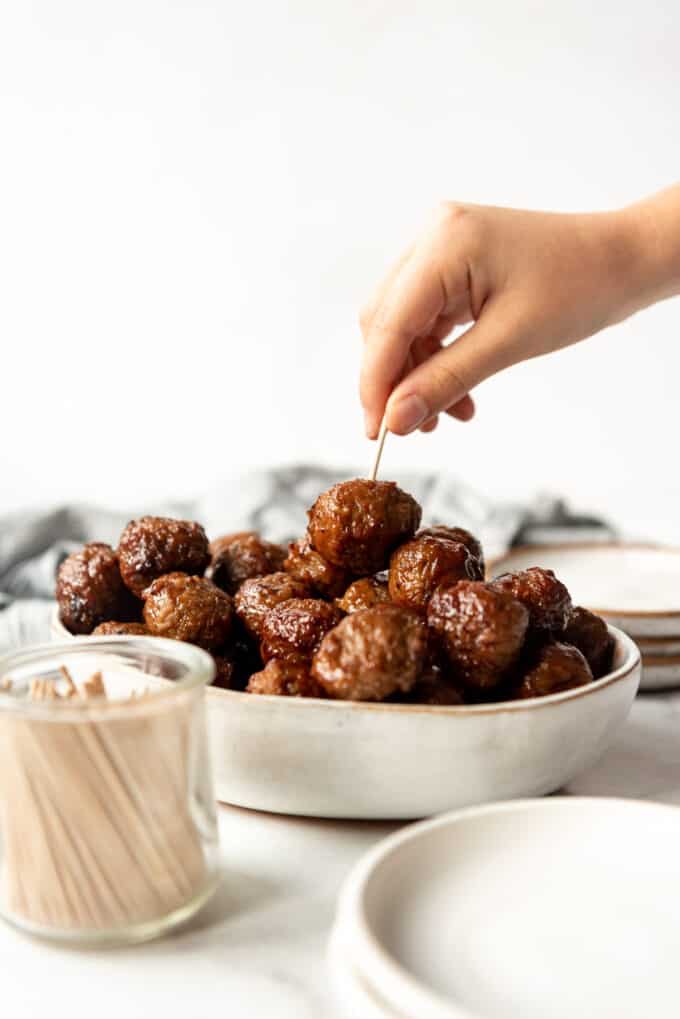 A hand picking up an easy bbq grape jelly meatball with a toothpick.