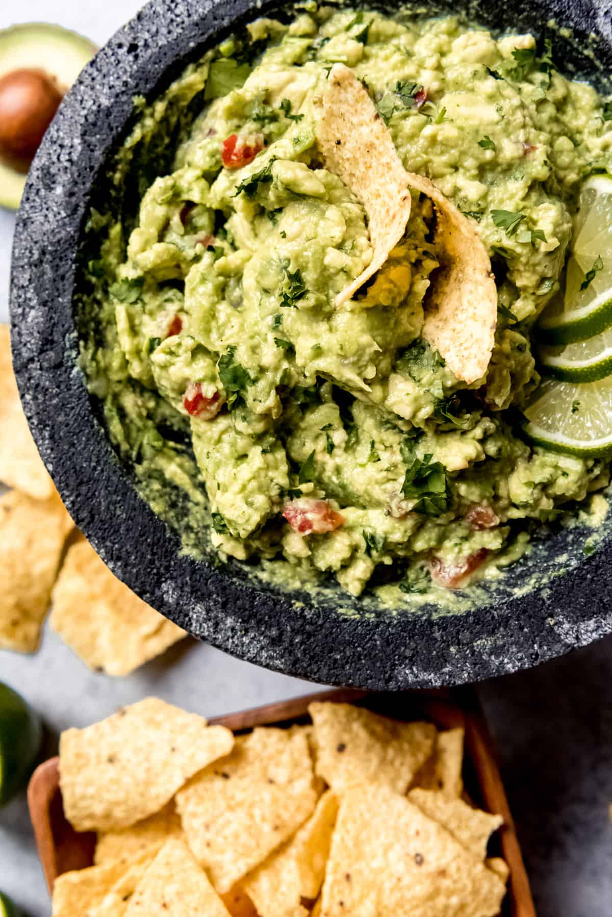 An image of homemade guacamole with cilantro and tomatoes in a stone molcajete.