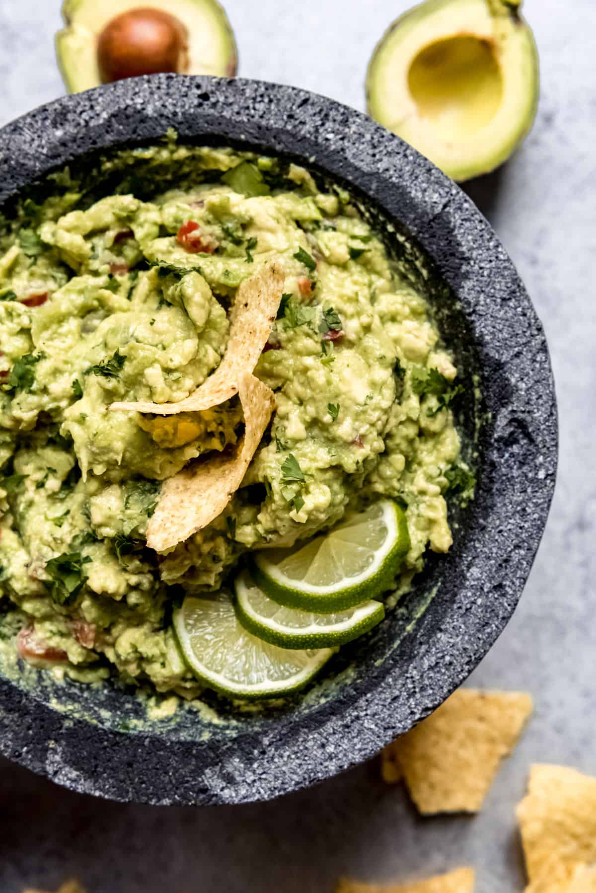 A bowl full of guacamole topped with tortilla chips and lime slices