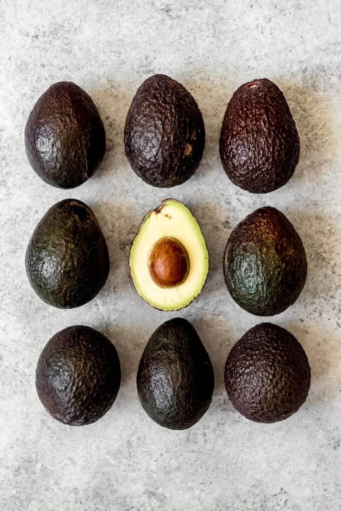 An image of an avocado with it's pit, surrounded by ripe avocados.