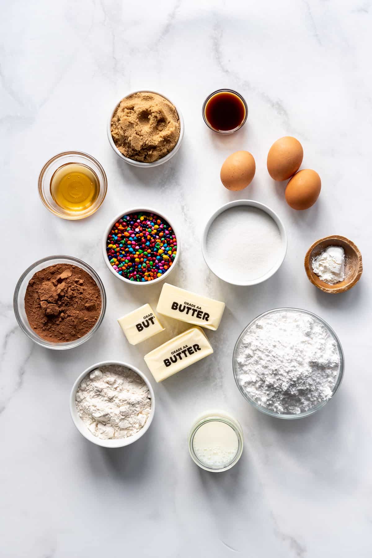 Ingredients for making homemade cosmic brownies in separate bowls on a white surface.