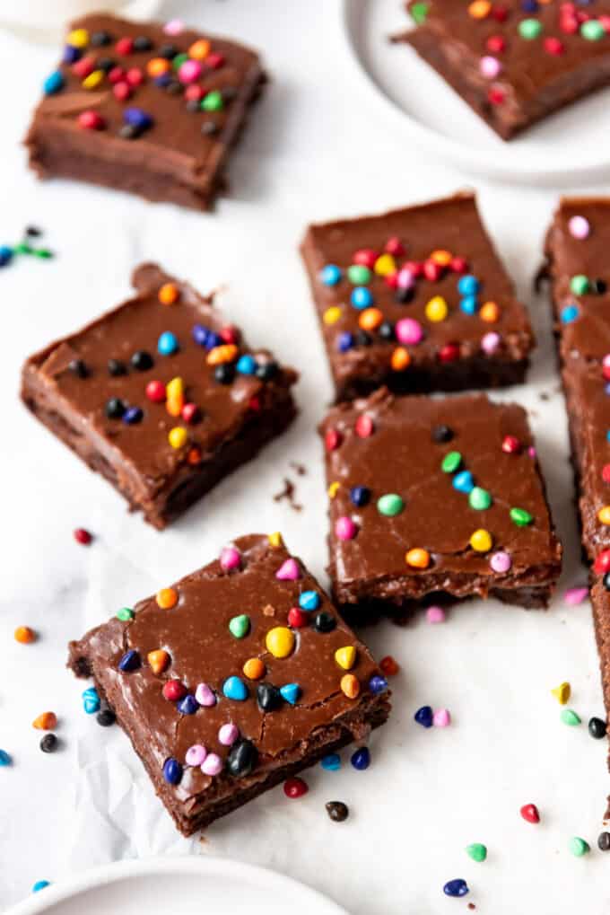Fudgy brownie squares with chocolate frosting and rainbow coated chocolate chips sprinkled on top.