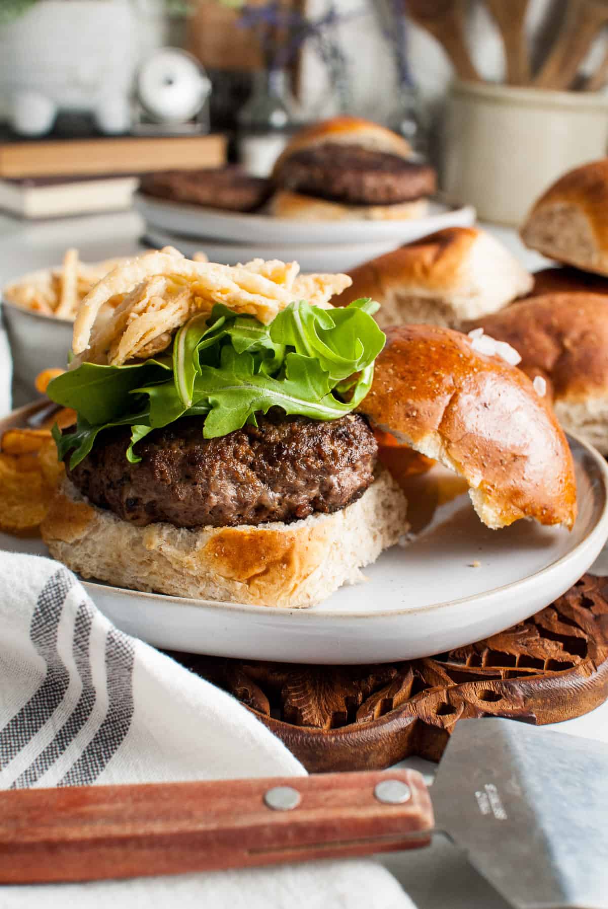 A burger topped with arugula and crispy fried onion strings on a plate.