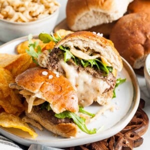 Two halves of a juicy lucy burger on a plate with potato chips.