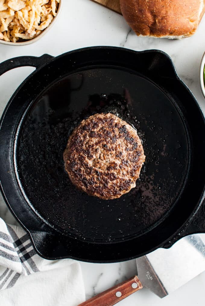 A close image of a juicy lucy hamburger patty being cooked on a cast iron skillet.