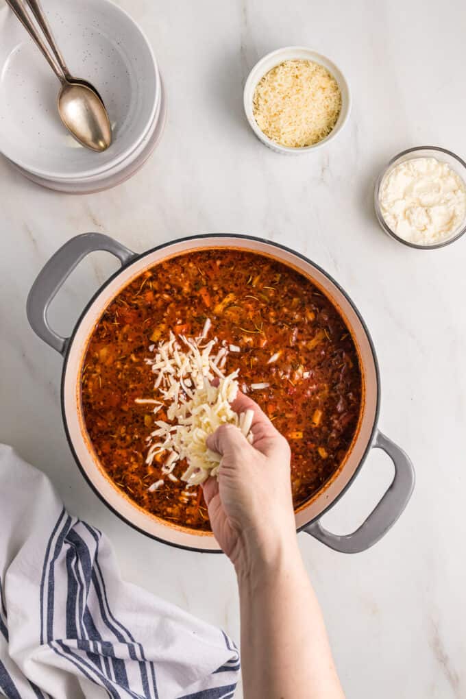 A hand sprinkling cheese into lasagna soup.