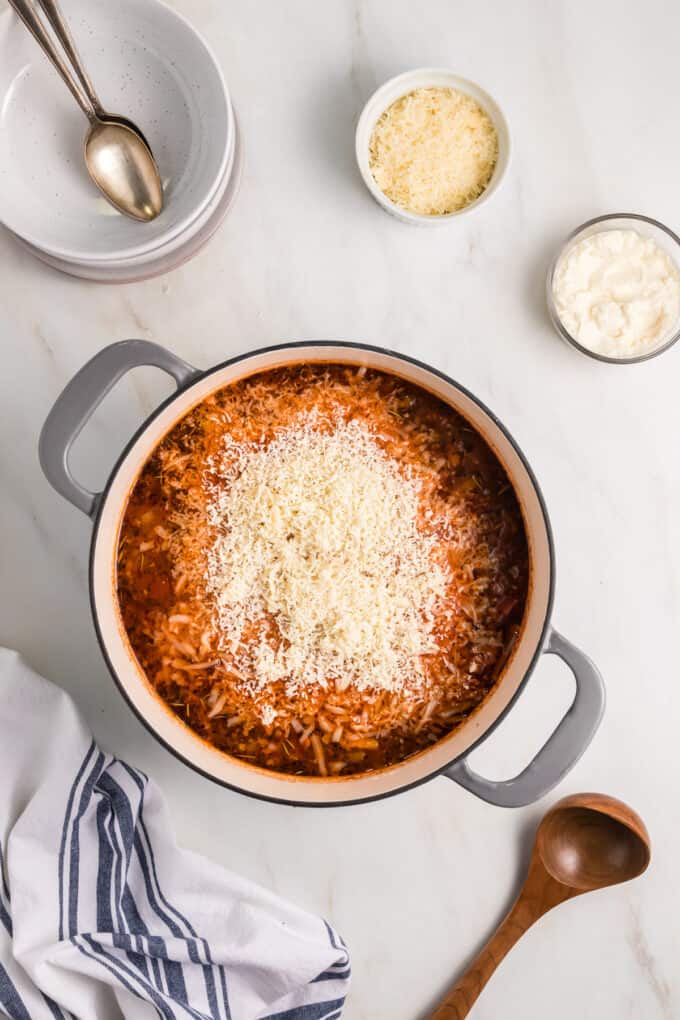 Grated parmesan and mozzarella cheese on top of a tomato based soup in a large pot.