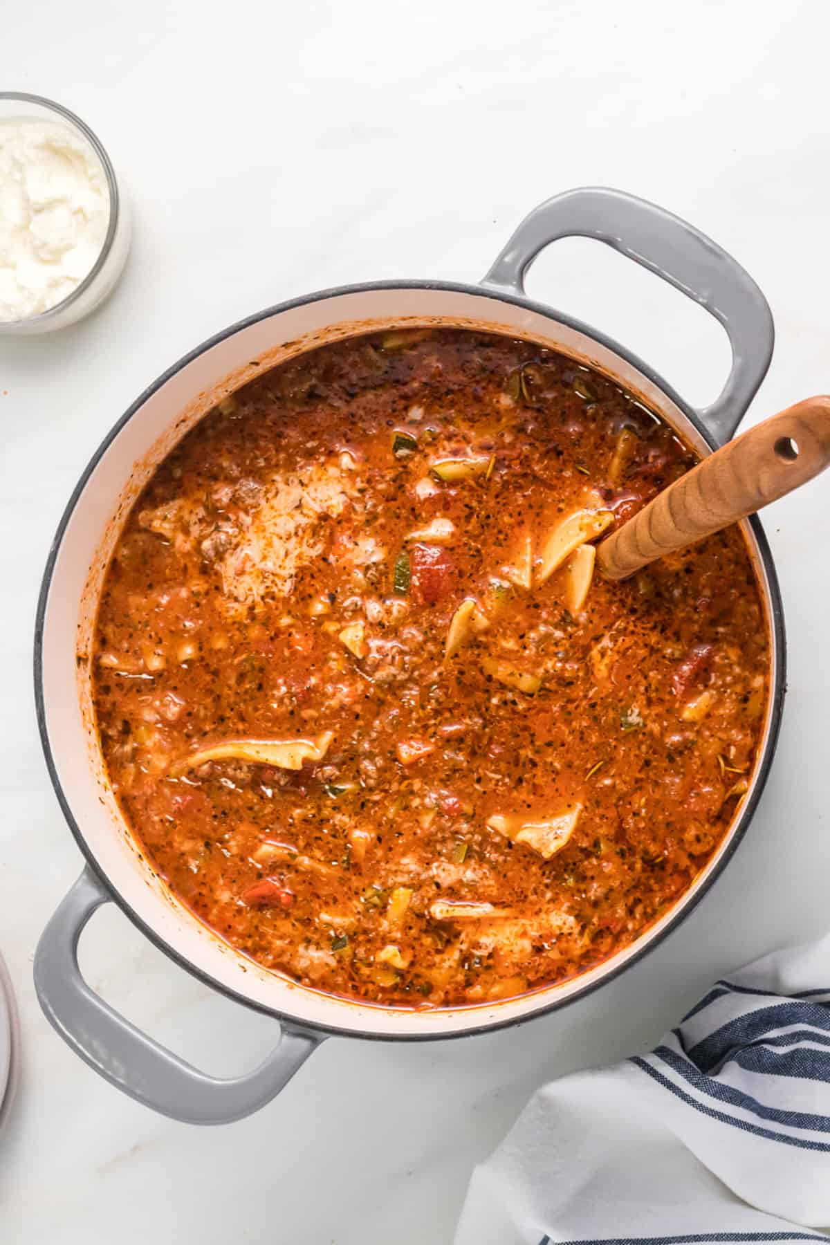 An overhead image of a pot of lasagna soup with a large wooden spoon in it.