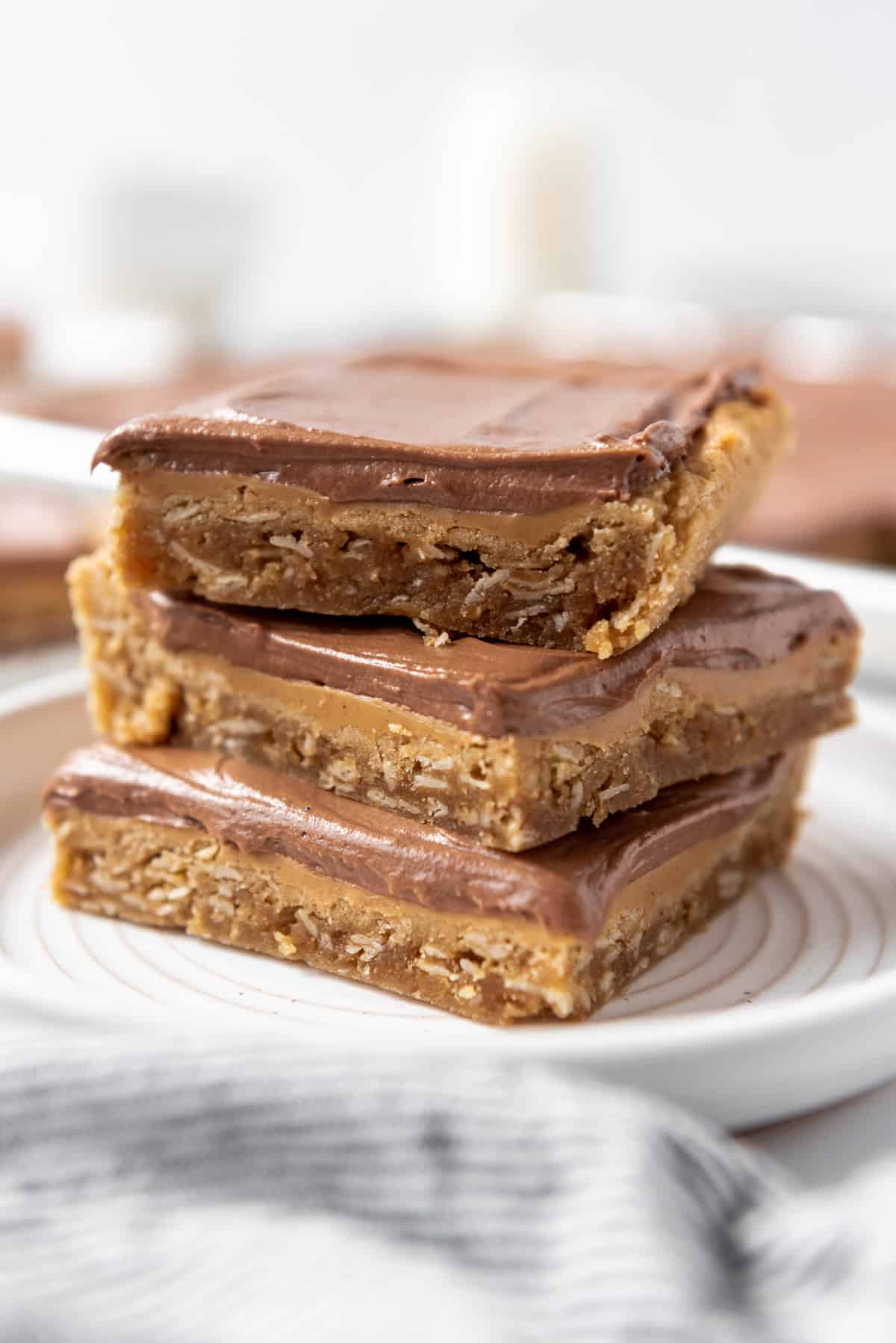 Three peanut butter bars with chocolate frosting stacked on a white plate.