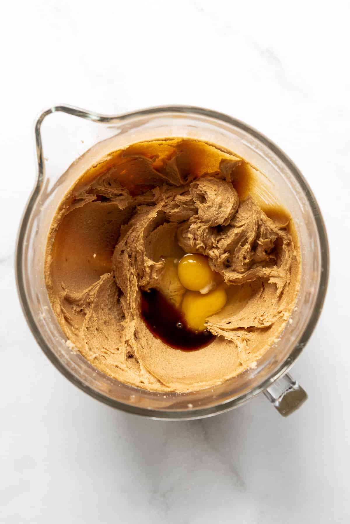 Adding eggs and vanilla extract to creamed peanut butter, sugar, and butter in a large glass mixing bowl.