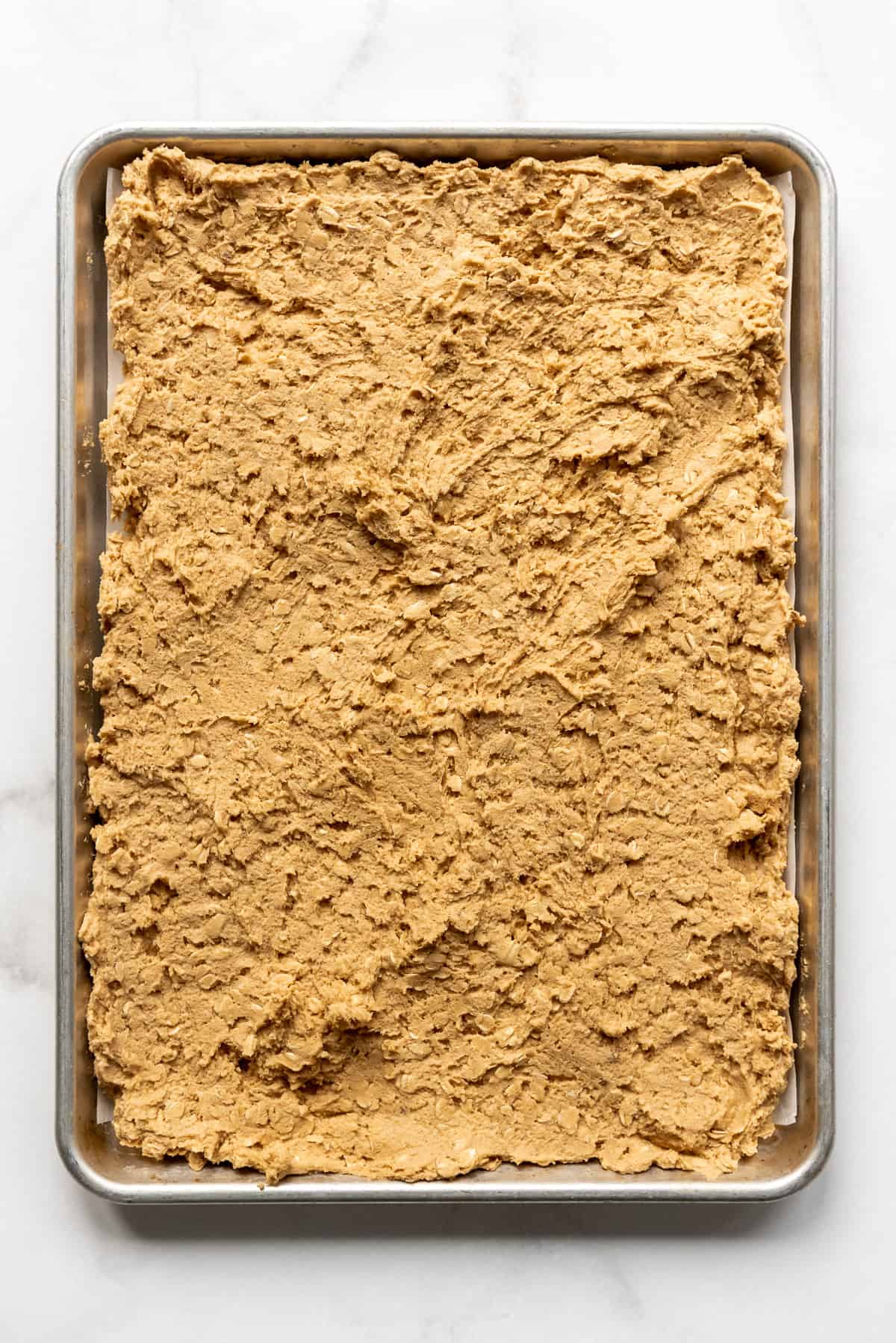 Soft peanut butter oatmeal cookie dough spread into a large baking sheet.