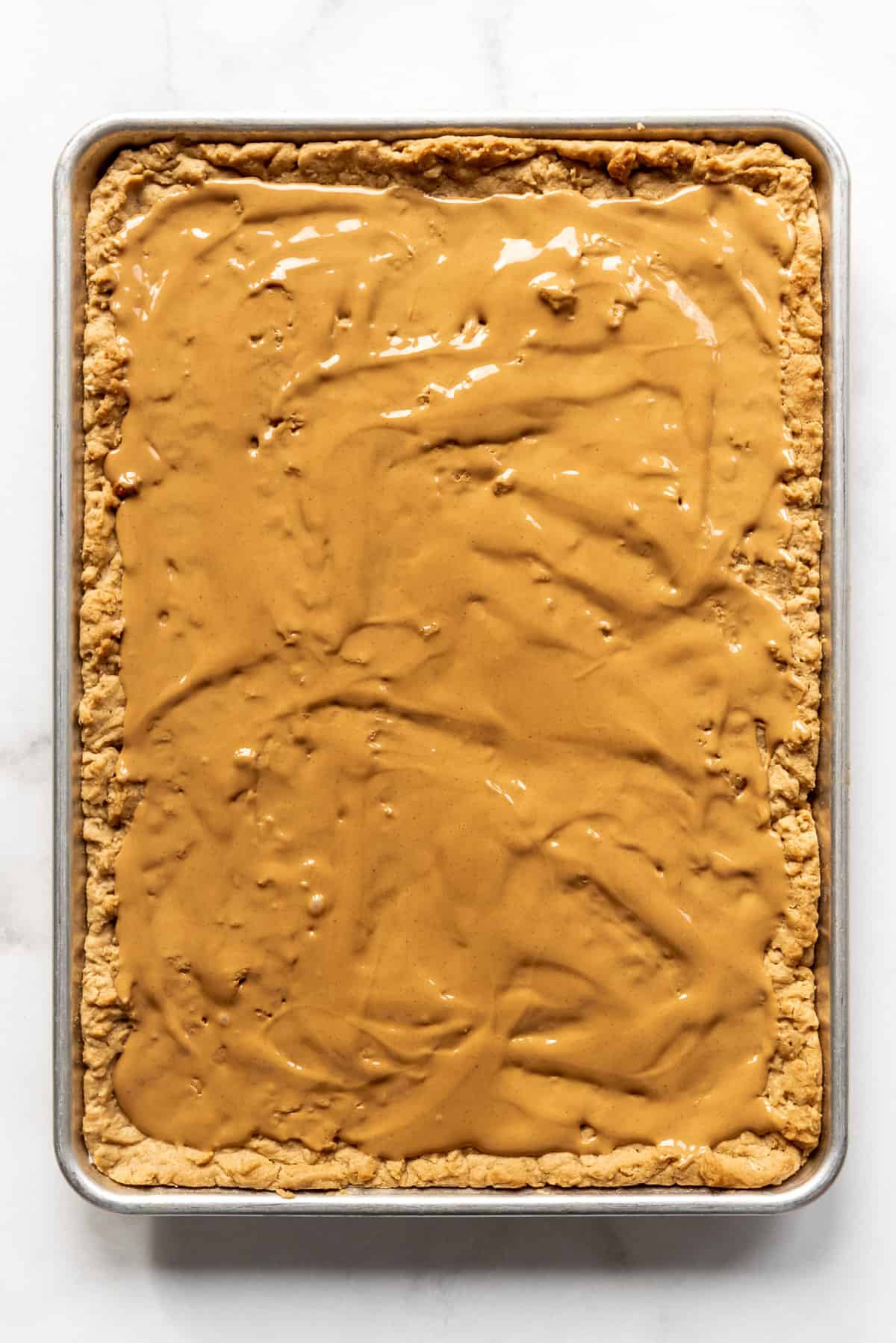 Melted peanut butter spread into a thin layer on top of warm peanut butter oatmeal bars in a large baking sheet.