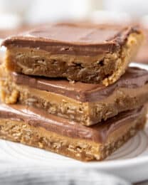 Three peanut butter bars with chocolate frosting stacked on a white plate.