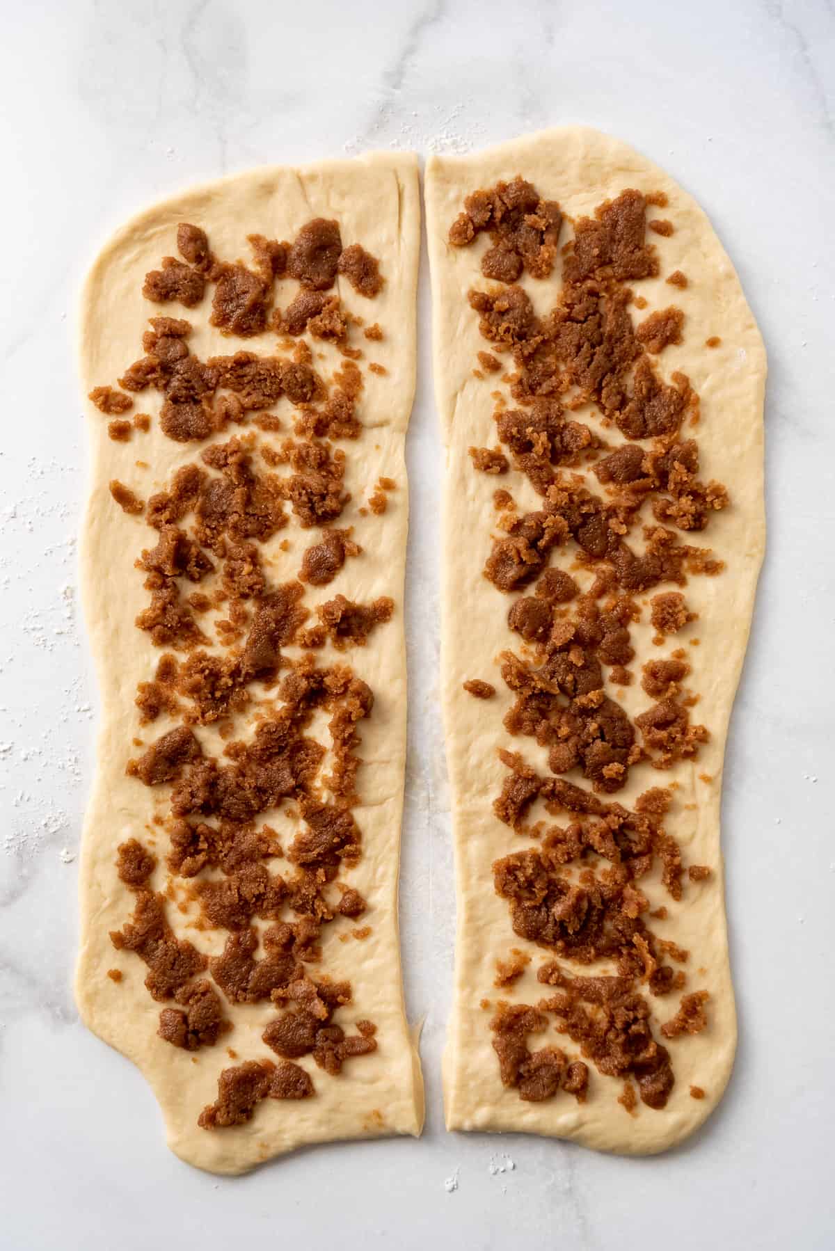 Sprinkling cinnamon sugar filling onto two long rectangles of brioche dough.