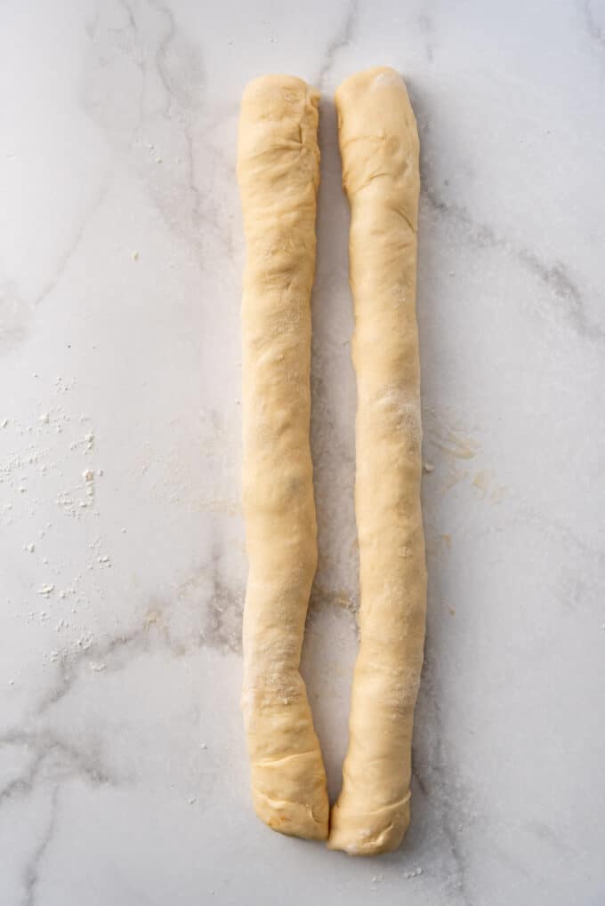 Two rolled up logs of soft brioche dough on a white surface.
