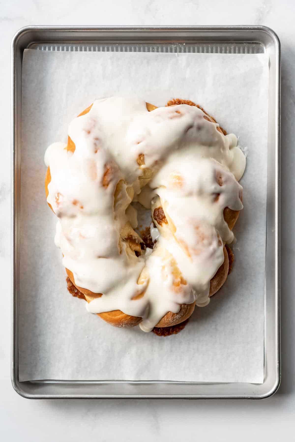 Adding simple frosting to a king cake on a baking sheet.