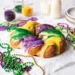 A homemade Mardi Gras king cake with jars of colored sugar in the background.