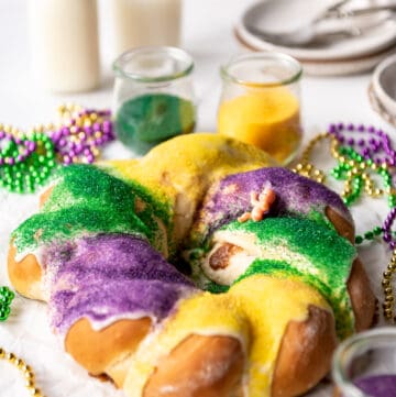 A homemade king cake covered with colored sugar in front of glasses of milk and plates.