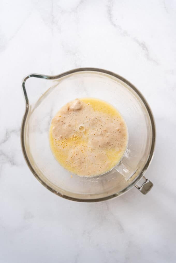 Proofed yeast in a glass bowl with melted butter, beaten eggs, and other ingredients.