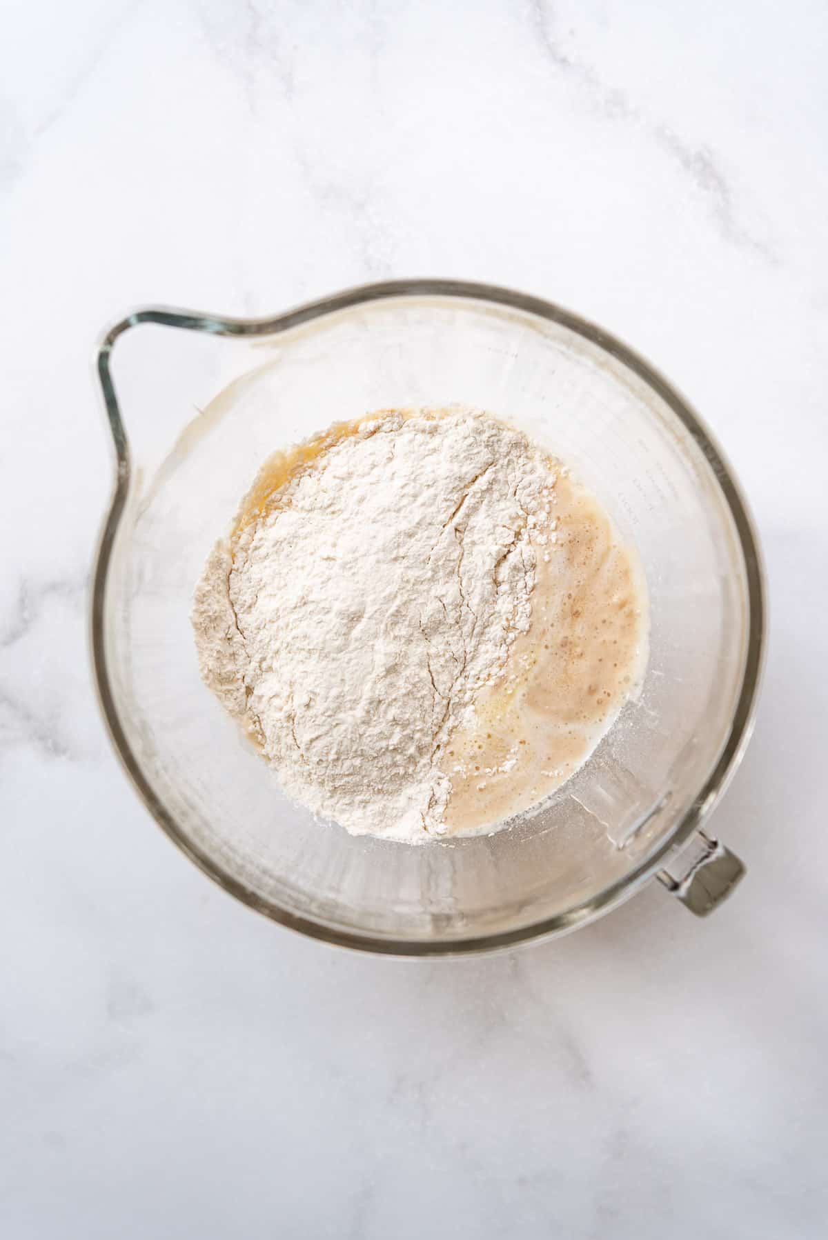 Adding flour to yeast, milk, sugar, and other ingredients in a bowl.