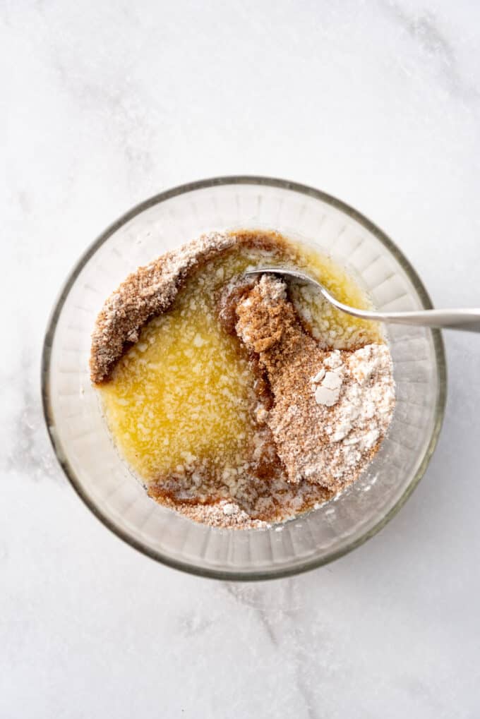 Mixing melted butter into cinnamon sugar filling in a glass bowl.
