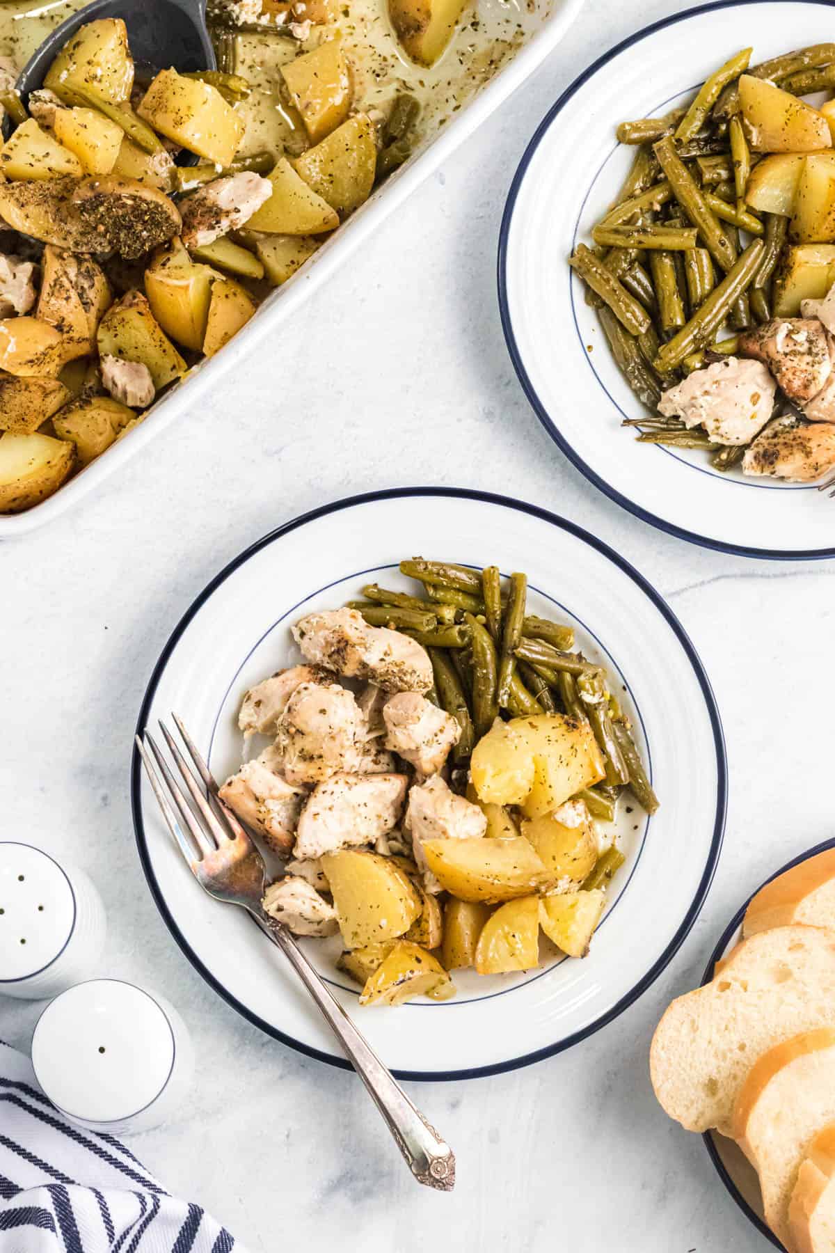 An overhead image of plates of oven roasted chicken breasts, potatoes, and green beans.