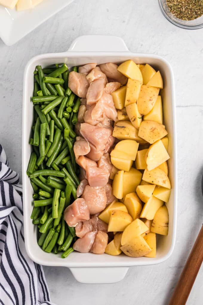 Arranging green beans, chicken chunks, and potato chunks in columns in a pan.